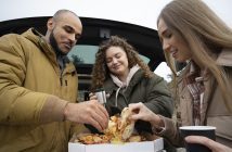 une famille mangeant des pizzas auprès de leur voiture