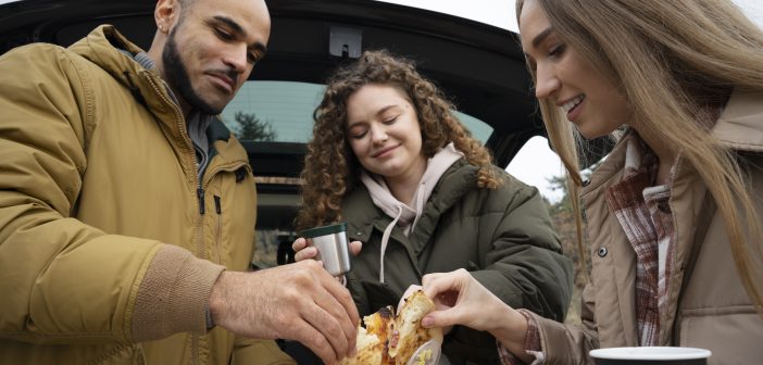 une famille mangeant des pizzas auprès de leur voiture